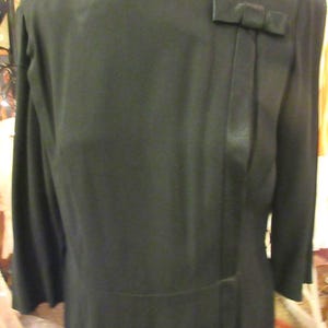 May include: A black long-sleeved dress with a satin bow detail on the shoulder and a single button closure.