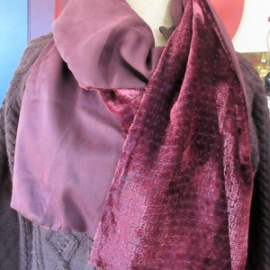 May include: A burgundy velvet scarf with a geometric pattern, paired with a solid burgundy silk scarf. The scarf is draped over a mannequin.