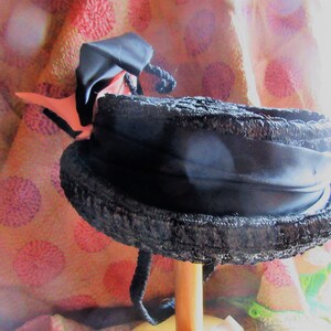 May include: A black straw hat with a wide brim and a black satin ribbon. The hat is decorated with a pink bow.