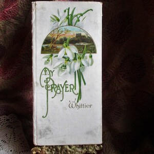 May include: A vintage book titled "My Prayer" by Whittier, with a floral design featuring white flowers and green leaves on the cover.