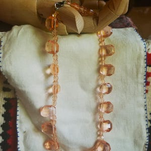 May include: A peach-coloured vintage necklace with faceted beads. The necklace is strung on a delicate chain and includes a matching bracelet. The beads are a mix of round and rectangular shapes, creating a unique and elegant design.