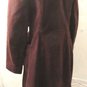 May include: A long brown suede coat with a white fur collar and trim. The coat has a long, flowing silhouette and a classic design.