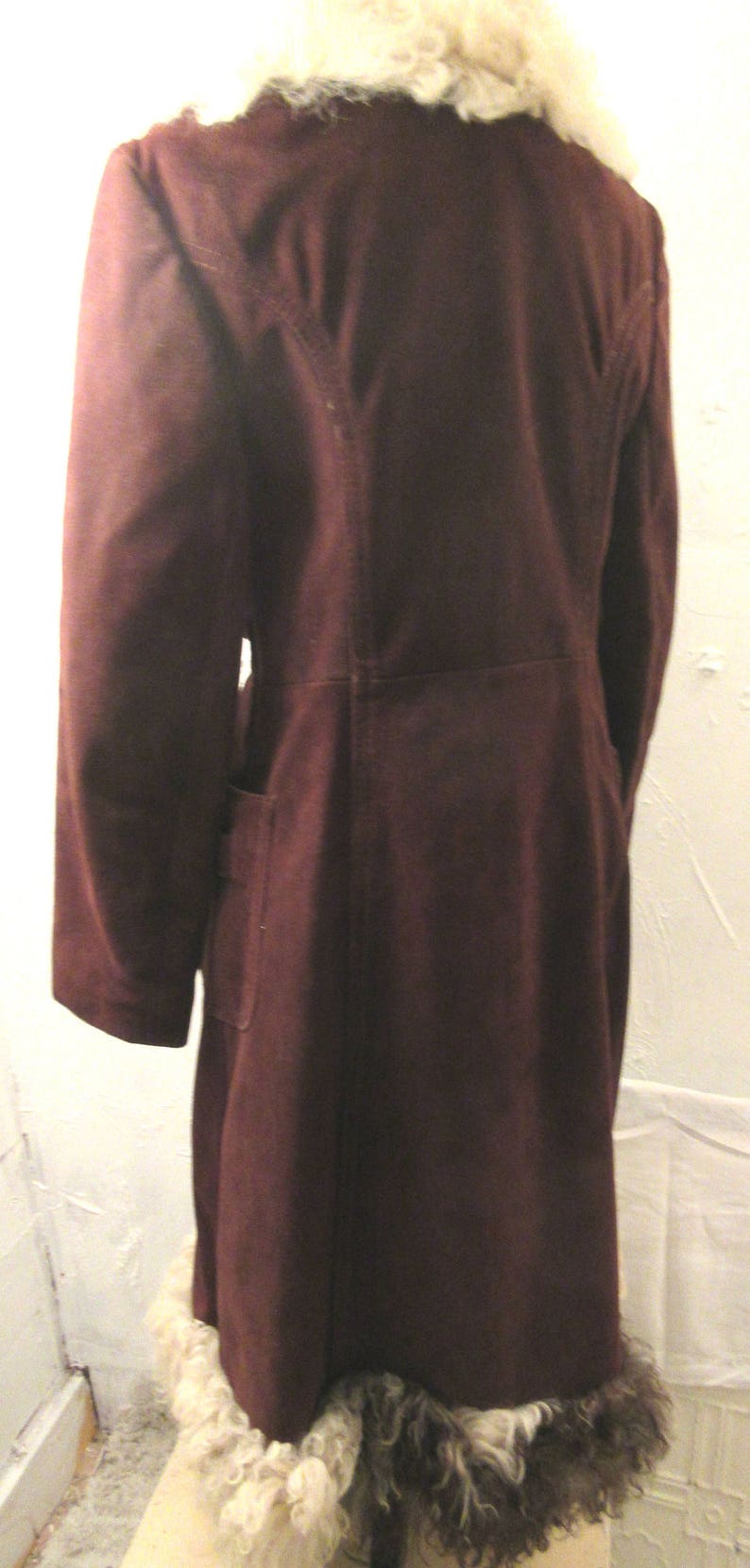 May include: A long brown suede coat with a white fur collar and trim. The coat has a long, flowing silhouette and a classic design.
