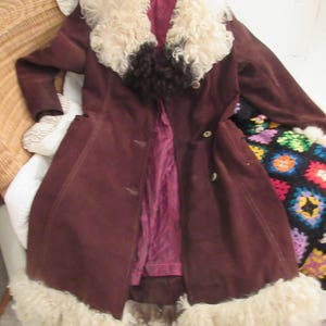 May include: A brown suede coat with a large white fur collar and trim. The coat has a button closure and a belt.