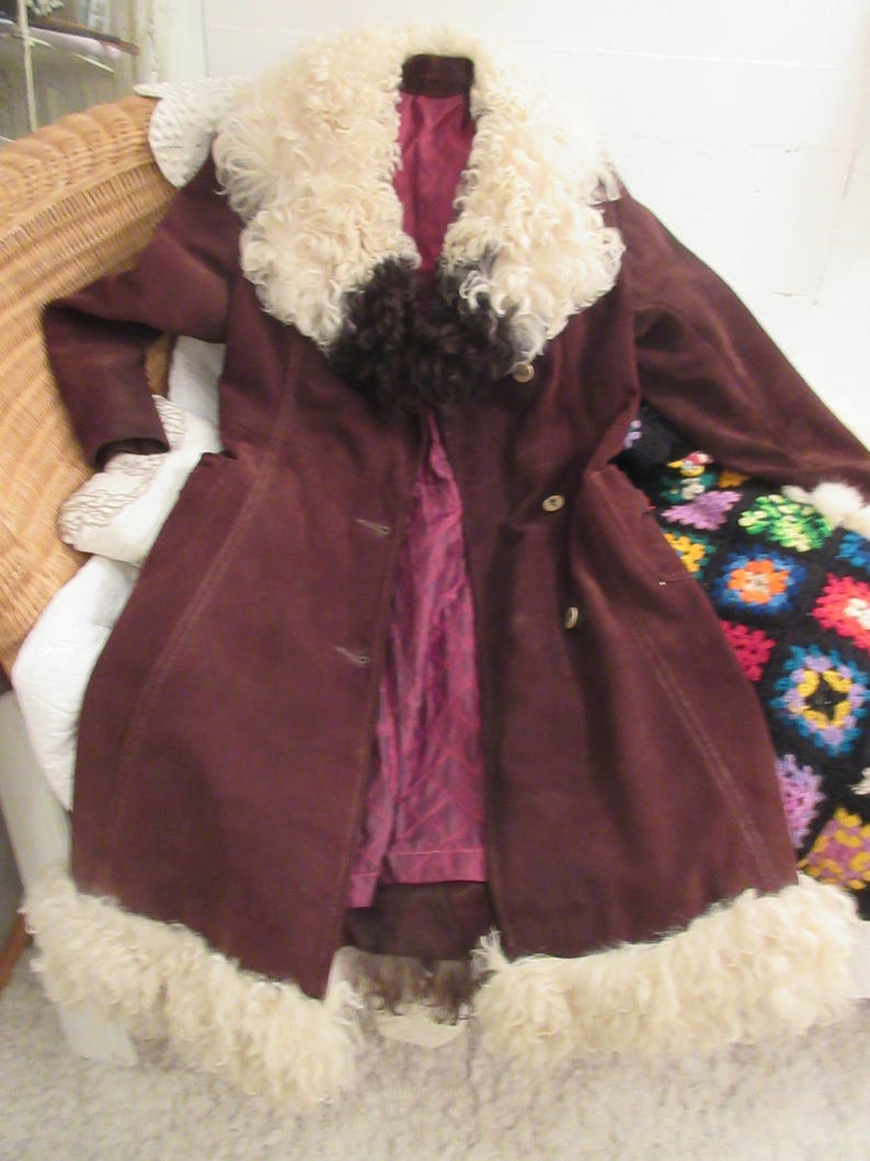 May include: A brown suede coat with a large white fur collar and trim. The coat has a button closure and a belt.