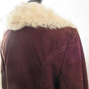 May include: A brown suede jacket with a white faux fur collar. The jacket has a seam down the back.