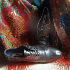 Peut inclure: Deux paires de chaussures à lacets en cuir noir avec des détails brogue. Les chaussures sont posées sur un tissu à motifs colorés.