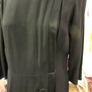 May include: A black dress with a satin trim and a bow at the neckline. The dress has a single button at the waist.