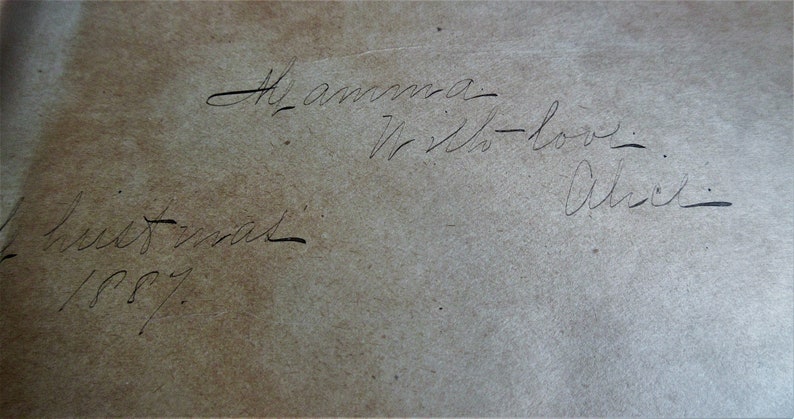 May include: A handwritten note on a light brown paper surface. The note reads 'To amma - With love - Alice - Christmas 1887.'