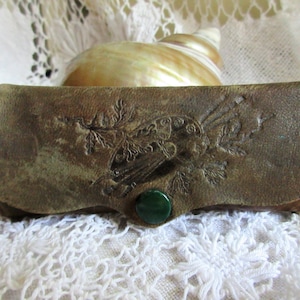 May include: A brown leather glasses case with an embossed design of a bird and foliage. The case has a green stone button closure.