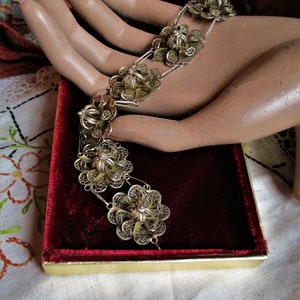 Può includere: Un braccialetto in filigrana d'argento con un design floreale. Il braccialetto è realizzato con un delicato e intricato lavoro di metallo e presenta una serie di maglie a forma di fiore collegate.
