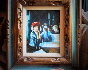 May include: An oil painting in a decorative frame depicts a scene in a restaurant. The painting features figures in a dimly lit setting, with a woman in a red hat as the focal point. The frame is a combination of gold, brown, and blue.