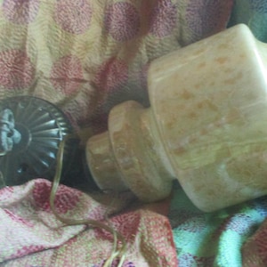 May include: A white ceramic lamp with a brown and white patterned base. The lamp has a white shade with a brown trim. The lamp is sitting on a patterned fabric.