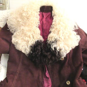 May include: A brown suede jacket with a large white and brown fur collar. The jacket has a button closure and a burgundy lining.