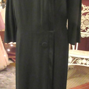 May include: A black dress with a long sleeve and a bow detail on the shoulder. The dress has a single button closure at the waist.