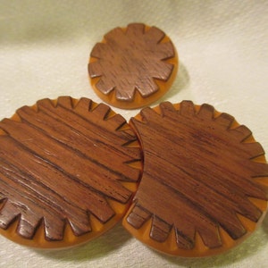 May include: Three round, brown and orange plastic buttons with a woodgrain pattern. The buttons have a scalloped edge.
