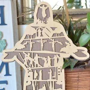 Op de afbeelding: Een houten uitsnijding van een persoon met verschillende scènes uit de Bijbel die in de figuur zijn gesneden. De uitsnijding staat op een houten tafel met een witte steen waarop het woord "LOVE" staat. De achtergrond is een houten muur met een bord waarop "HOME" staat.