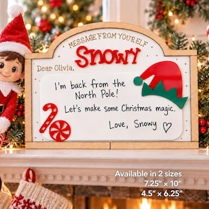 May include: A wooden sign with the text MESSAGE FROM YOUR ELF, SNOWY, Dear Olivia, I'm back from the North Pole! Let's make some Christmas magic. Love, Snowy, featuring a red and green elf hat and candy cane. Available in 7.25" x 10" and 4.5" x 6.25".