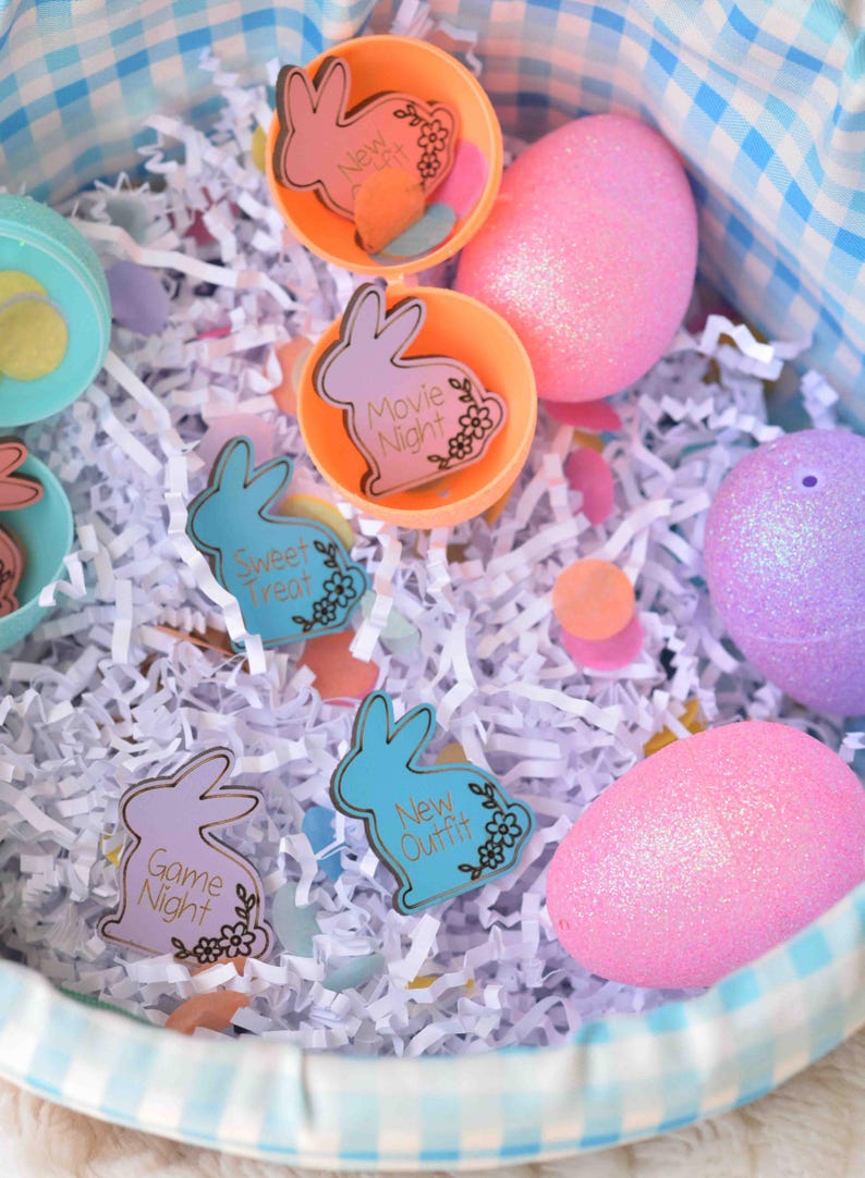 May include: An Easter basket filled with colorful eggs and decorative bunny-shaped tags. The tags have phrases like "Movie Night" and "New Outfit". The basket is lined with white paper and has a blue and white checkered pattern.