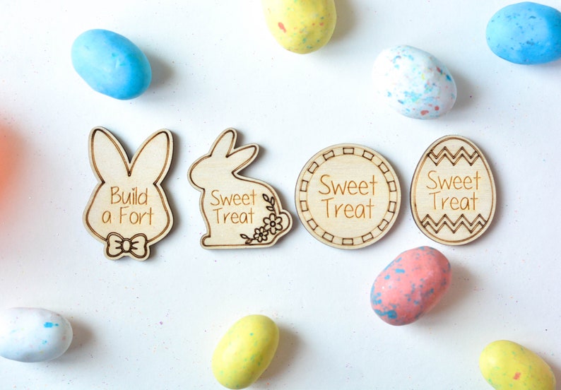 May include: Wooden Easter-themed decorations with the phrases "Build a Fort" and "Sweet Treat" engraved on them. The decorations include bunny and egg shapes, and are surrounded by colorful Easter egg candies.