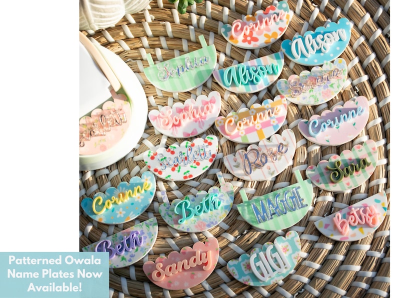 Puede incluir: Una colecci&oacute;n de placas con nombres estampados con varios nombres en escritura cursiva, incluyendo "Corinne" y "Allison". Las placas tienen bordes festoneados y est&aacute;n dispuestas sobre una superficie tejida. El texto "Patterned Owala Name Plates Now Available!" es visible.