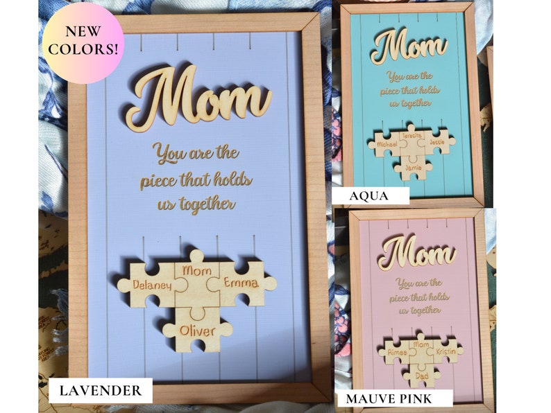 Puede incluir: Letrero enmarcado de madera con la palabra "Mom" en cursiva y la frase "You are the piece that holds us together". Debajo, un rompecabezas de madera con nombres. Disponible en lavanda, aguamarina y rosa malva.