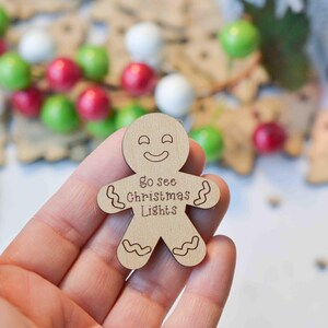K&ouml;nnte beinhalten: Ein Holz-Lebkuchenmann-Anh&auml;nger mit einem l&auml;chelnden Gesicht und dem Text "go see Christmas Lights".