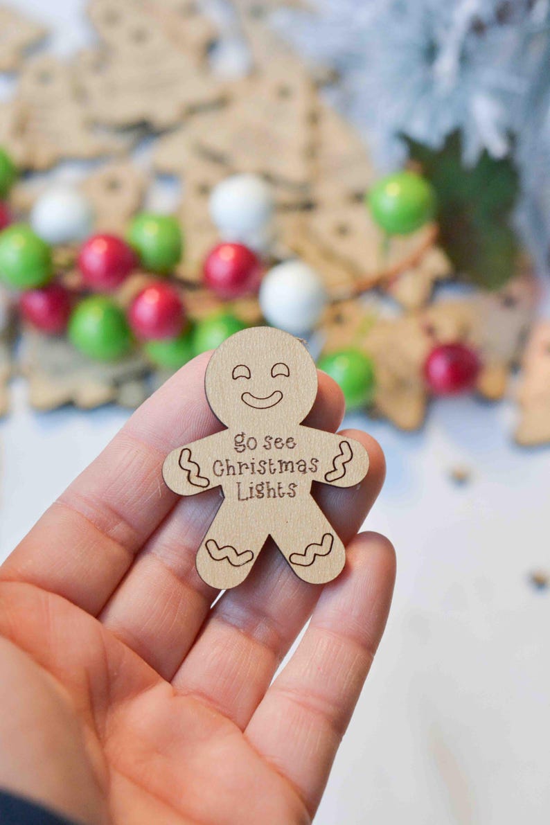 K&ouml;nnte beinhalten: Ein Holz-Lebkuchenmann-Anh&auml;nger mit einem l&auml;chelnden Gesicht und dem Text "go see Christmas Lights".
