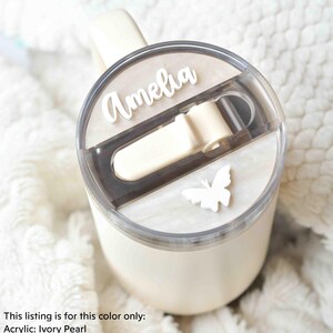 May include: A white tumbler with a clear lid and a butterfly design. The lid has a sliding closure and the tumbler is personalized with the name "Amelia".
