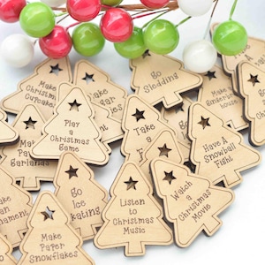 K&ouml;nnte beinhalten: Ein Haufen aus Holz geschnitzter Weihnachtsbaum-Anh&auml;nger mit verschiedenen festlichen Aktivit&auml;ten, die darauf geschrieben sind, wie "Schlittschuhlaufen gehen", "Papier-Schneeflocken basteln", "Weihnachtsmusik h&ouml;ren", "Einen Weihnachtsfilm schauen", "Eine Schneeballschlacht machen", "Eine Pause einlegen", "Schlitten fahren", "Ein Lebkuchenhaus bauen", "Ein Weihnachts-Spiel spielen", "Weihnachts-Cupcakes backen", "Eine Girlande basteln" und "Zuckerpl&auml;tzchen backen".