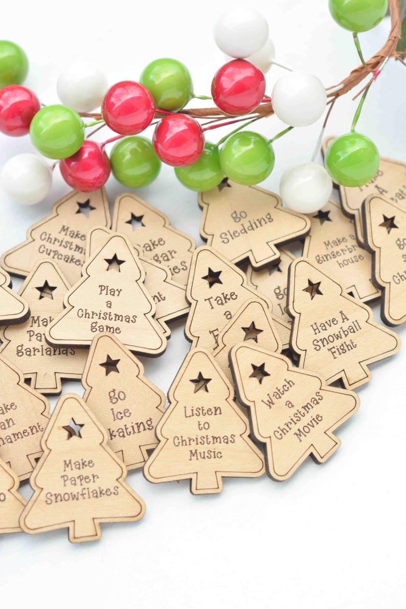 K&ouml;nnte beinhalten: Ein Haufen aus Holz geschnitzter Weihnachtsbaum-Anh&auml;nger mit verschiedenen festlichen Aktivit&auml;ten, die darauf geschrieben sind, wie "Schlittschuhlaufen gehen", "Papier-Schneeflocken basteln", "Weihnachtsmusik h&ouml;ren", "Einen Weihnachtsfilm schauen", "Eine Schneeballschlacht machen", "Eine Pause einlegen", "Schlitten fahren", "Ein Lebkuchenhaus bauen", "Ein Weihnachts-Spiel spielen", "Weihnachts-Cupcakes backen", "Eine Girlande basteln" und "Zuckerpl&auml;tzchen backen".