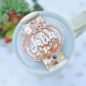 May include: A white and gold glitter pumpkin-shaped tumbler lid with the name "Julia" written in white on top.