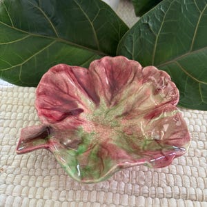 May include: A small ceramic dish shaped like a flower petal with a glossy finish. The surface features a blend of deep pink, magenta, and light green colors with a visible fine crackle glaze pattern throughout the entire piece of pottery.
