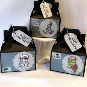 May include: Three black Halloween gift boxes with tags. Each box has a different design: a witch's hat, a skull and crossbones, and a cartoon zombie. The tags say "Happy Halloween".