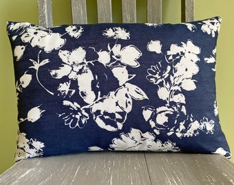May include: Rectangular decorative pillow with a navy blue background and a white floral pattern. The pillow is made of a textured fabric and is placed on a gray wooden chair.