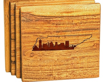 Puede incluir: Conjunto de cuatro posavasos de madera con una silueta del horizonte de Nashville dentro del contorno del estado de Tennessee. Los posavasos están hechos de madera natural de color marrón claro con un patrón de veta de madera.