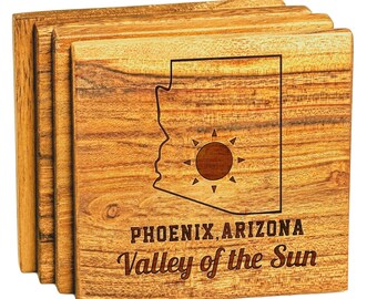 Può includere: Set di quattro sottobicchieri in legno con un contorno inciso a laser dell'Arizona con un sole al suo interno. I sottobicchieri sono in legno di acacia e hanno il testo "PHOENIX, ARIZONA Valley of the Sun" inciso sul fondo.