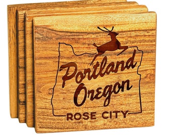 Może przedstawiać: Zestaw czterech drewnianych podkładek pod kubki z sylwetką jelenia skaczącego nad obrysem stanu Oregon. Podkładki są grawerowane tekstem "Portland Oregon - Rose City".