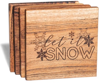 Può includere: Set di quattro sottobicchieri in legno con finitura in legno naturale. I sottobicchieri presentano un design inciso a laser con fiocchi di neve e il testo "Let it Snow".