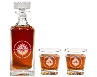 May include: A clear glass decanter with a compass design etched on the front, filled with amber liquid. Two matching clear glass tumblers with the same compass design are also included.