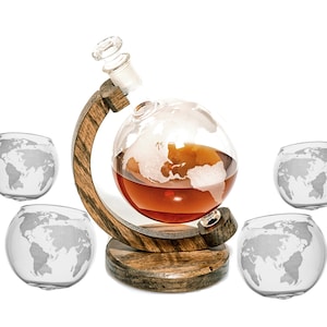 May include: A wooden globe decanter with a clear glass globe and a brown liquid inside. The decanter is surrounded by four clear glass globe shot glasses with a world map etched on the bottom.