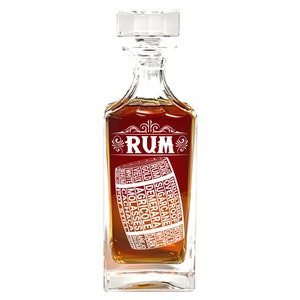 May include: A clear glass decanter with a stopper, filled with amber liquid. The decanter has a white design of a barrel with the word "RUM" and various types of rum listed around the barrel.