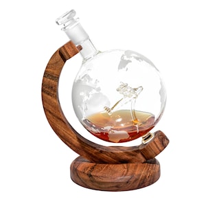 May include: A clear glass globe decanter with a world map etched on the surface, filled with amber liquid. The decanter sits on a wooden stand shaped like a globe, with a dark brown finish.