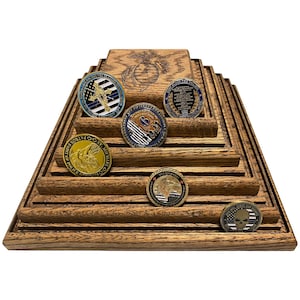 May include: A wooden display stand with five tiers for displaying challenge coins. The stand is made of dark wood with a natural grain pattern. The coins are arranged on the tiers, with the top tier featuring a coin with a Marine Corps emblem. The coins feature various designs, including a police officer, a skull, and a flag.