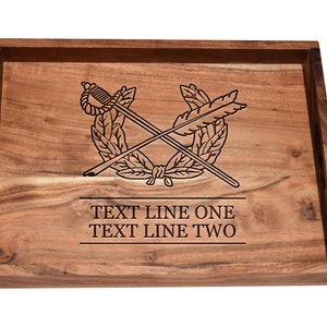 May include: A rectangular wooden tray with a dark brown finish. The tray features an engraved design of crossed swords and a wreath, with the text "TEXT LINE ONE" and "TEXT LINE TWO" below the design. The tray has a raised edge.