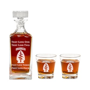 May include: A set of three clear glass decanter and glasses with a military theme. The decanter and glasses are filled with a dark amber liquid. The decanter has the text "TEXT LINE ONE TEXT LINE TWO AIRBORNE TEXT LINE THREE TEXT LINE FOUR" and a stylized image of a lightning bolt and dagger. The glasses have the text "AIRBORNE" and the same stylized image.