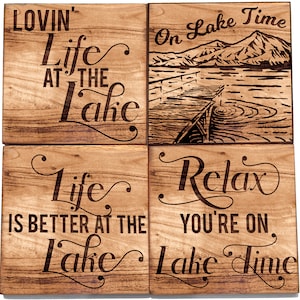 May include: Four square wooden coasters with lake-themed phrases and imagery. One coaster reads "Lovin' Life at the Lake," another depicts a lake scene with a dock, and the others say "Life is better at the Lake" and "Relax, You're on Lake Time."