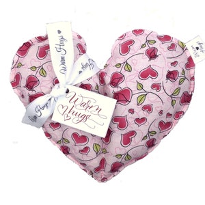 May include: Pink heart-shaped fabric pouch with a floral pattern of pink roses and hearts. The pouch has a white ribbon tied around it with a tag that says "Warm Hugs".