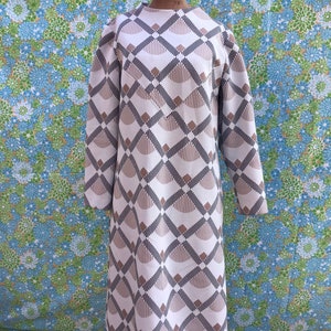 Puede incluir: Un vestido blanco de manga larga con un patrón geométrico en marrón y negro. El vestido tiene un escote redondo y una falda ligeramente acampanada.