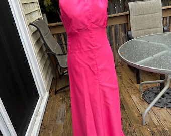 May include: A hot pink sleeveless maxi dress with a high neck and a fitted bodice. The dress has a simple design and is made of a smooth fabric.
